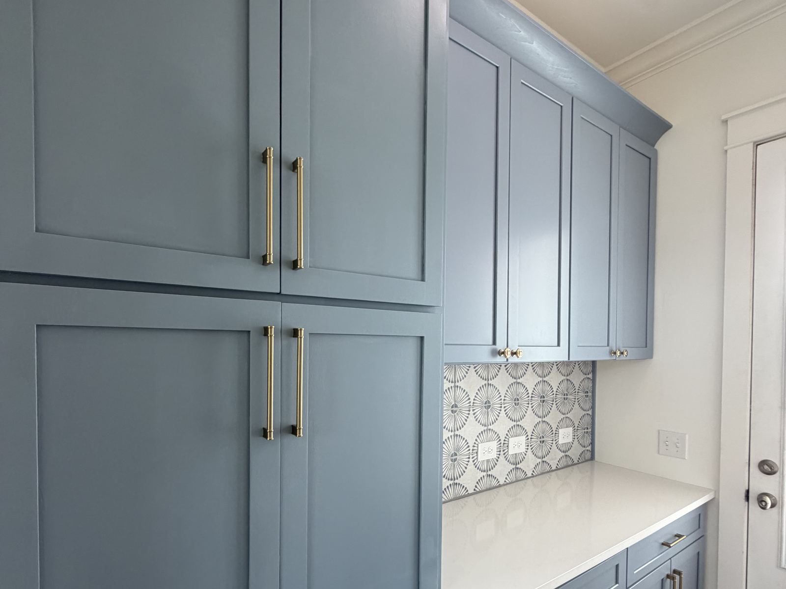 Custom butler's pantry with painted cabinetry, brass hardware, patterned tile backsplash, and a quartz counter