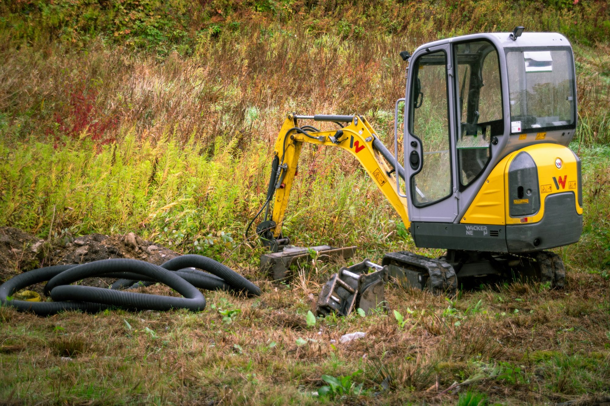 A mini excavator next to a coil of perforated drain pipe
