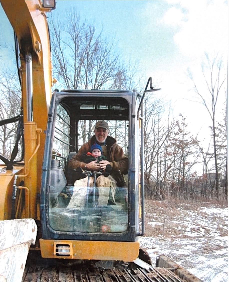 Josiah as a small child sitting in an excavator cab on his Uncle Donnie's lap