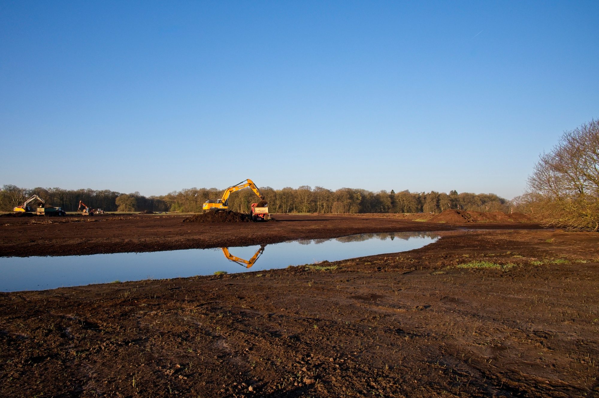 An excavator beside a newly dug pond on flat open ground